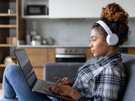 Woman at home watching conference on her laptop using headphones
